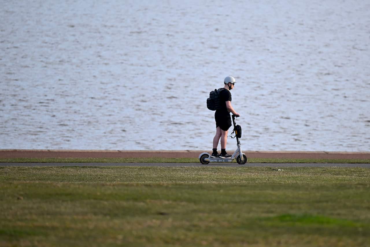 A man rides his e-scooter near the shore of Lake Burley-Griffin in Canberra.