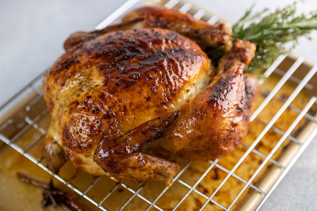 A golden brown roast chicken sits on a rack over a silver baking tray.