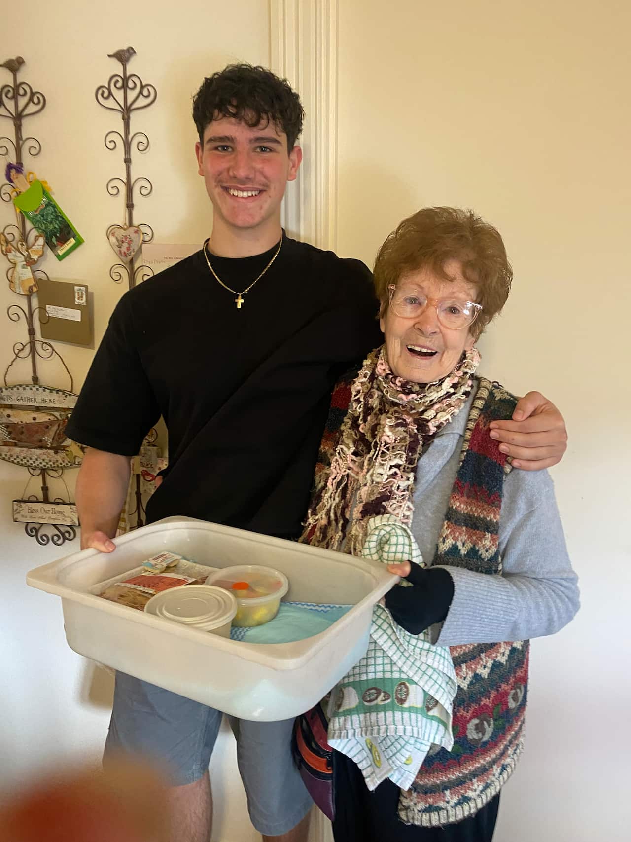 A man in a black shirt and a woman in grey shirt and knitted scarf hold a white tray with boxes inside